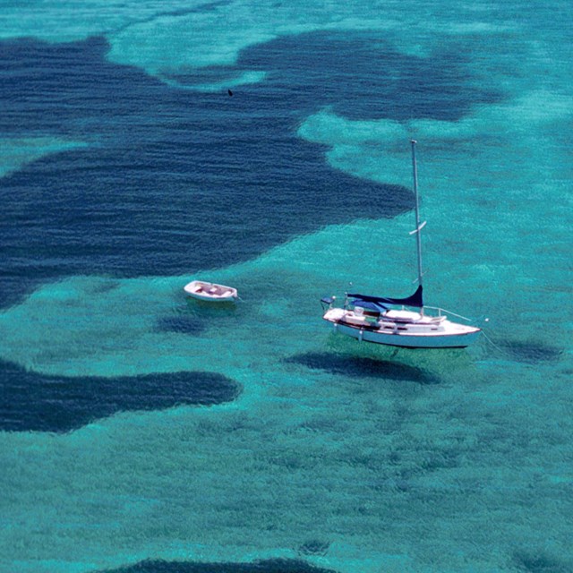 A large sail boat and a small boat floating on clear water