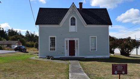 A man holds an Ebey's Forever Fund sign in front of a newly renovated historic home.