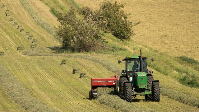 A tractor bales alfalfa in a patchwork of green fields.