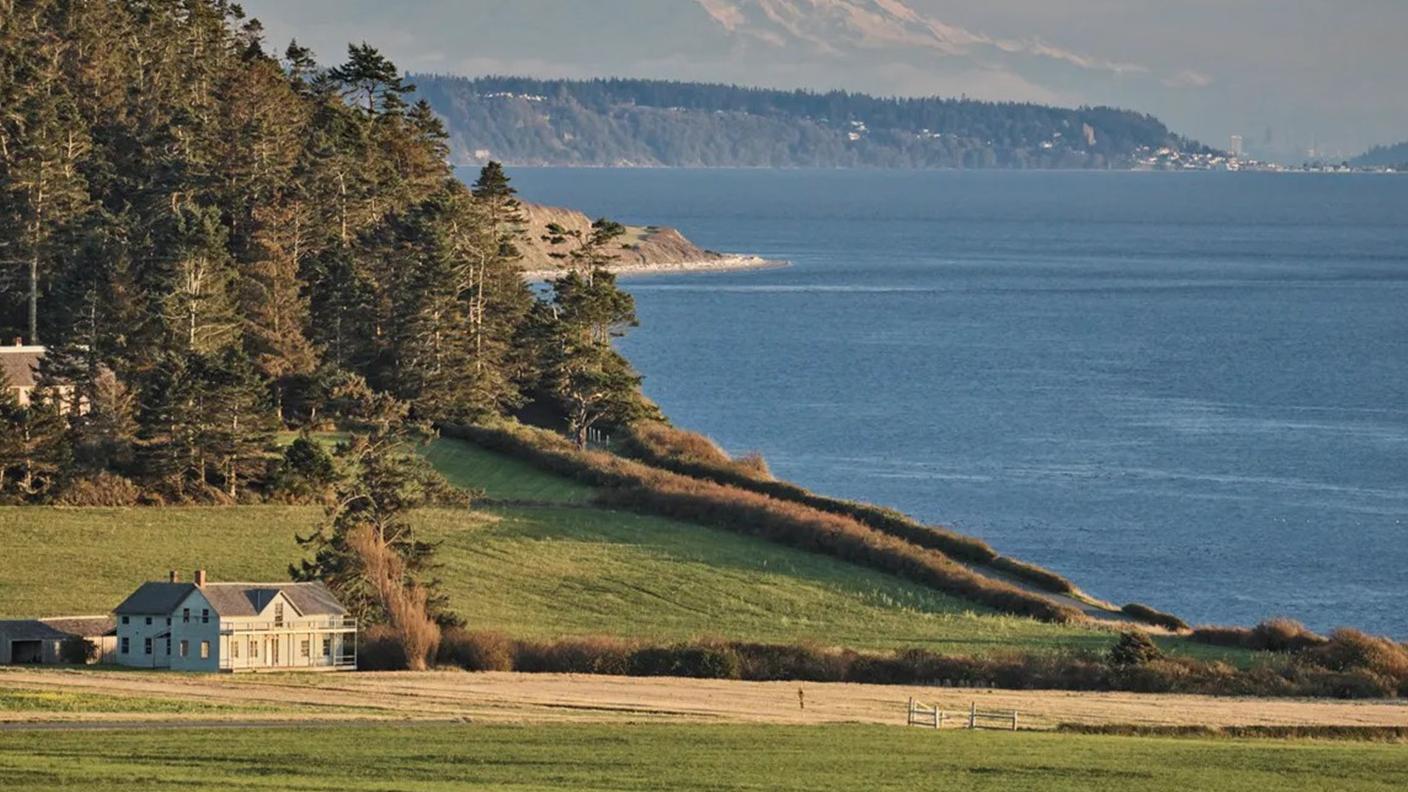 A house sitting in grassy fields with mountains and an ocean view in the background