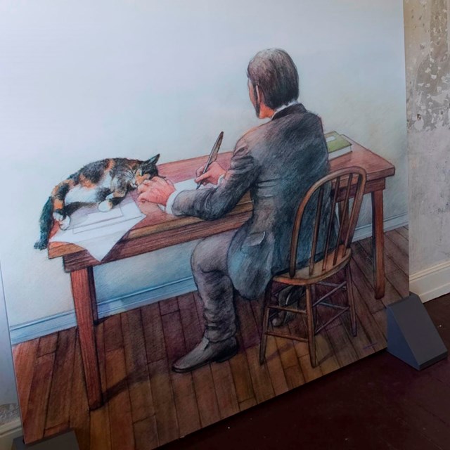 Color photo of a wall mural showing a man writing on a desk with a cat nearby.
