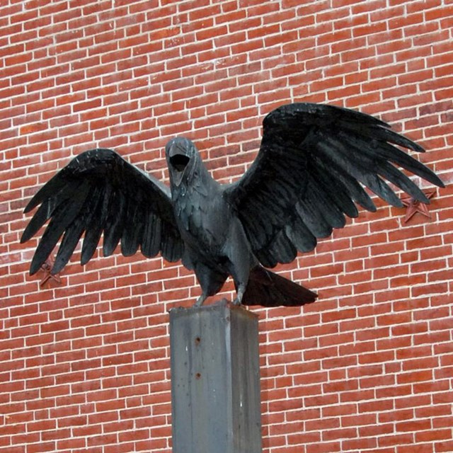 Color photo of a raven statue with wings outspread on a plinth.