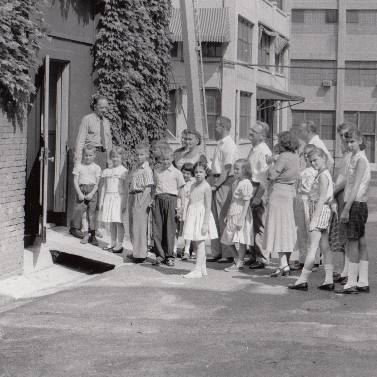 A park ranger leads a group into a lab structure (black and white, historic photo)