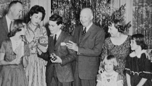 A black and white image of several people gathered together in front of a Christmas tree. 