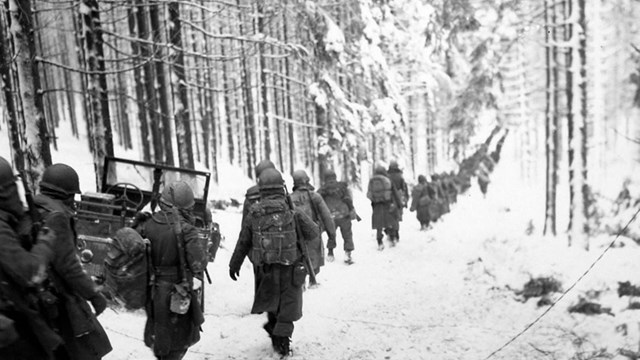 A black and white photograph showing a row of soldiers marching in a snowy forest