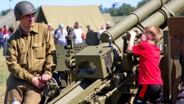 A young visitor in a red shirt looks through the site on a WWII artillery piece