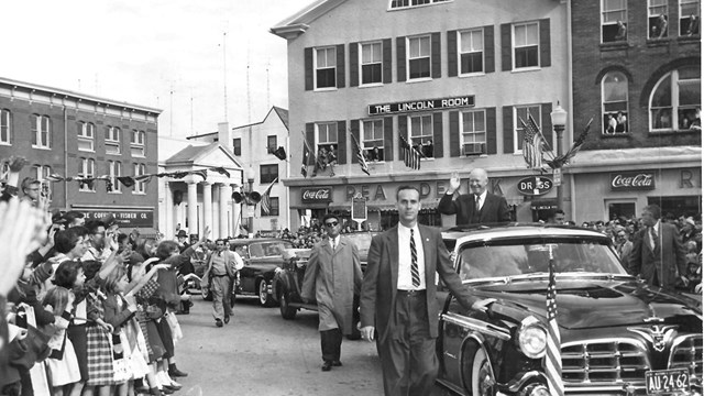 Black and white image of President Eisenhower driving through the Gettysburg town square