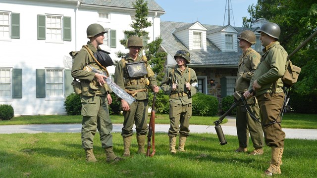 Volunteers in WWII uniforms stand in front of the Eisenhower home.