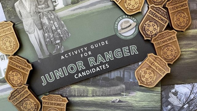 A color image of a green and black Junior Ranger book with wooden badges