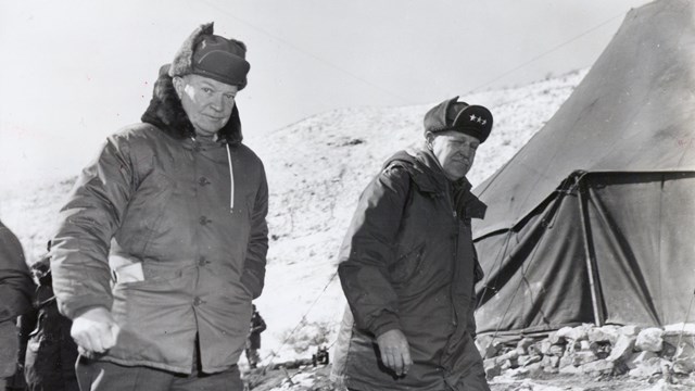 A black and white image showing Eisenhower walking in winter gear in Korea