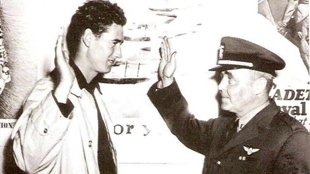 Two men, one in military uniform, stand side by side while holding their right hands in the air