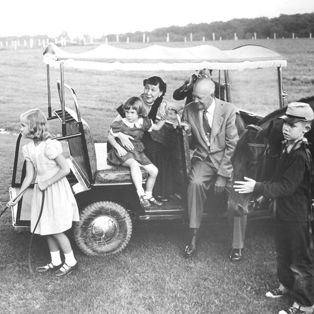 A black and white image of several Eisenhower family members gathered around a golf cart