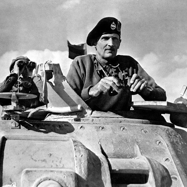 A black and white image of a man standing in a tank and holding binoculars