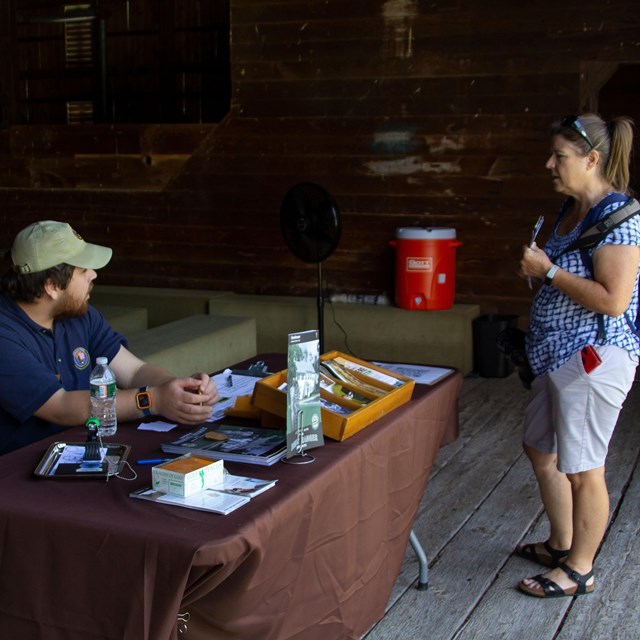 A visitor speaking with an intern at an information table inside a barn.
