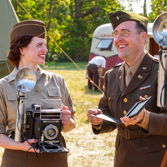 Two living history volunteers stand next to each other with historic camera equipment