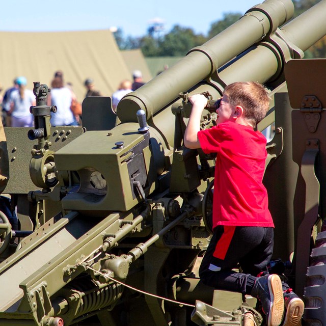 A young visitor in a red shirt looks through the site on a WWII artillery piece