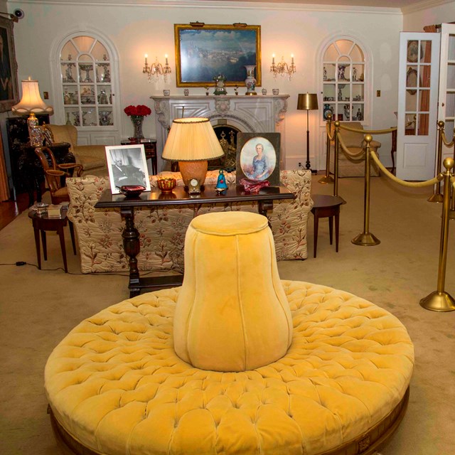 The formal living room in the Eisenhower home features a large circular yellow couch and cabinets.