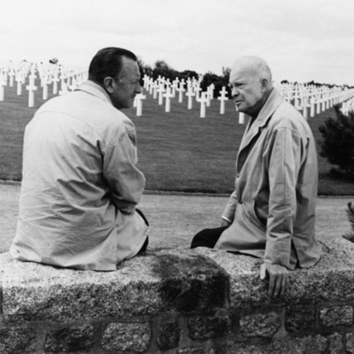 A black and white image showing two men sitting on a stone wall
