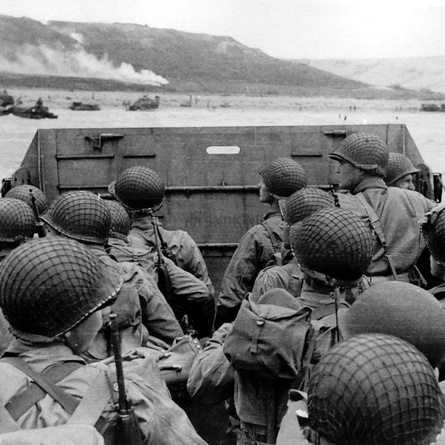 A black and white image of soldiers on a landing craft approaching the shores of Normandy