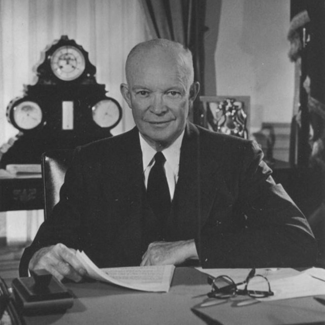 A black and white picture of a man in a suit sitting at a desk