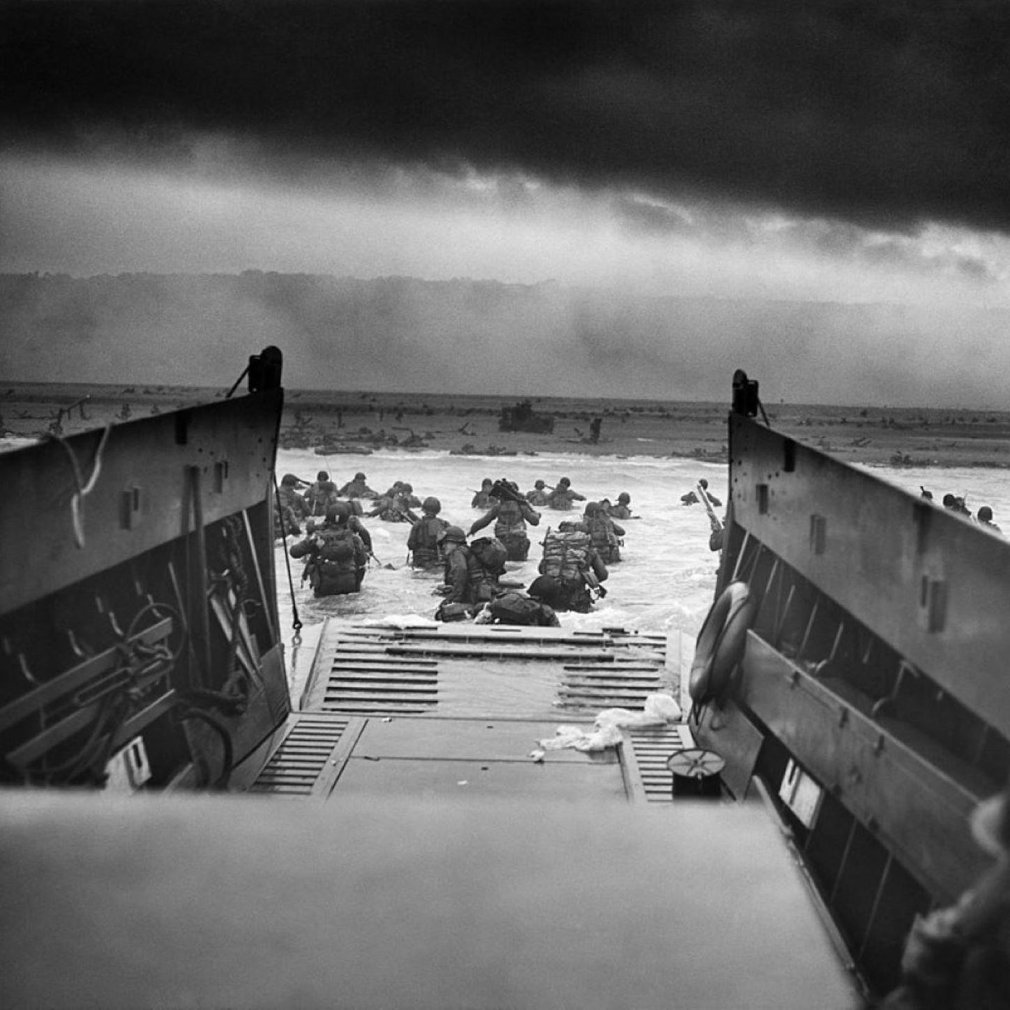 A black and white image showing men wading ashore from a boat