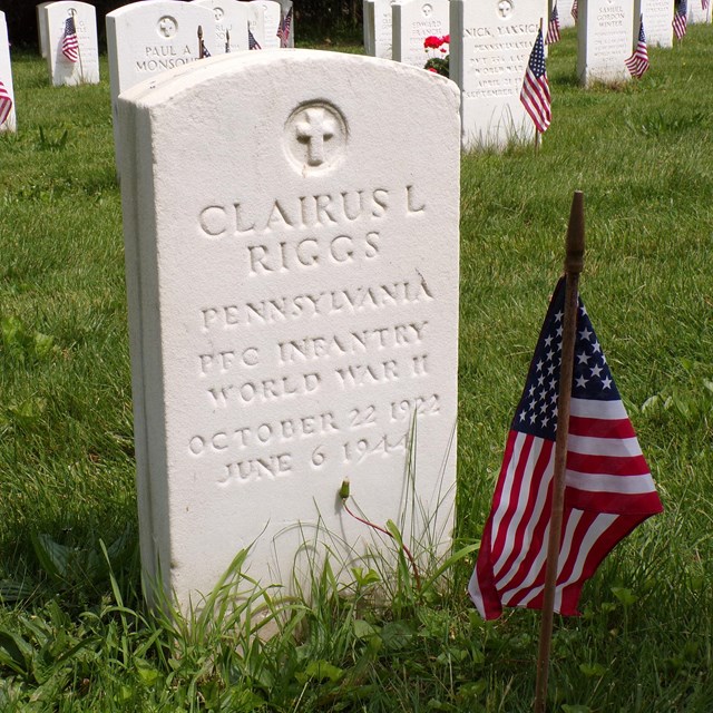An image of a white headstone with an American flag in front