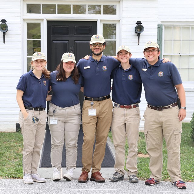 A group of interns wearing blue polo shirts pose in front of the Eisenhower home.