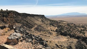 A long dirt road winds down a steep escarpment that drops off into a vast desert.