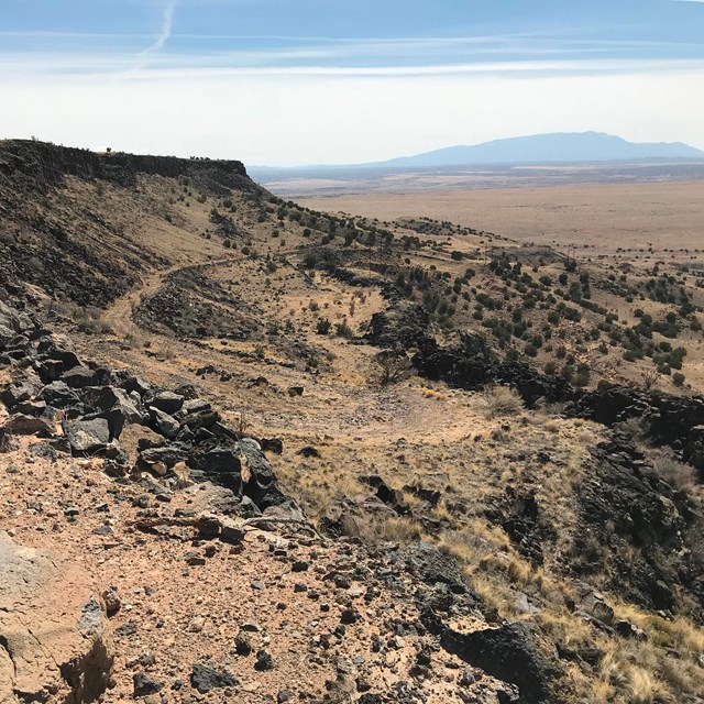 A long dirt road winds down a steep escarpment that drops off into a vast desert.