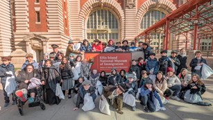 Students dressed as immigrants 100 years ago in front of the Ellis Island sign.