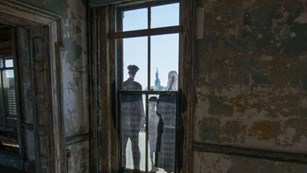Life size historic photo of family in doorway of stabilized building gazing at the Statue of Liberty