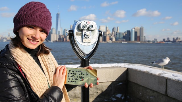 Visitor holding gold brick with message in Italian standing on Ellis Island on New York Harbor.