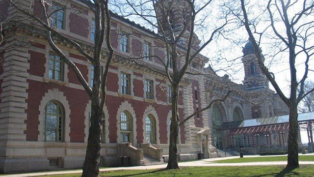 The main building on Ellis Island seen behind trees from the lawn