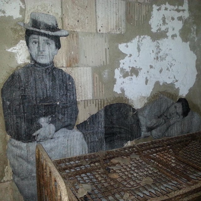Photo of immigrant next to an old bed frame.