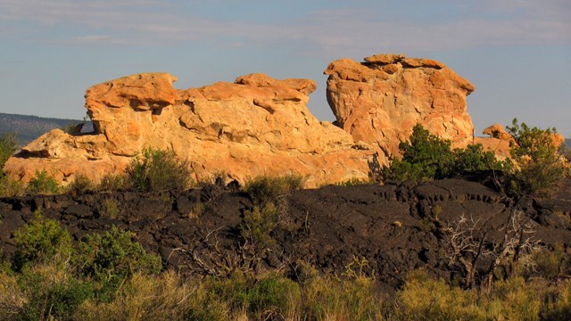 A cliff of sandstone rises above dark lava rock