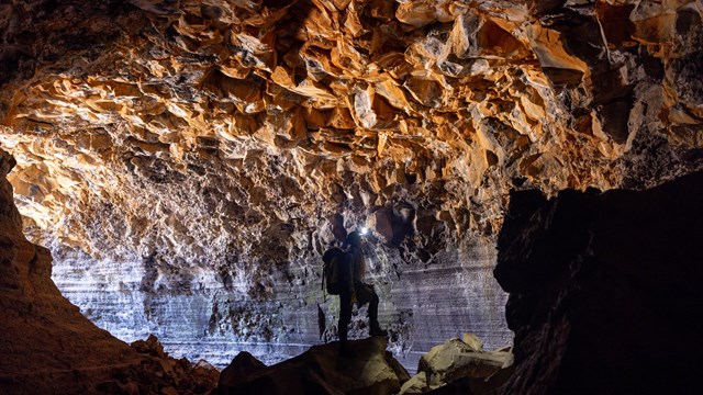 A caver is silhouetted against a lit cave background.