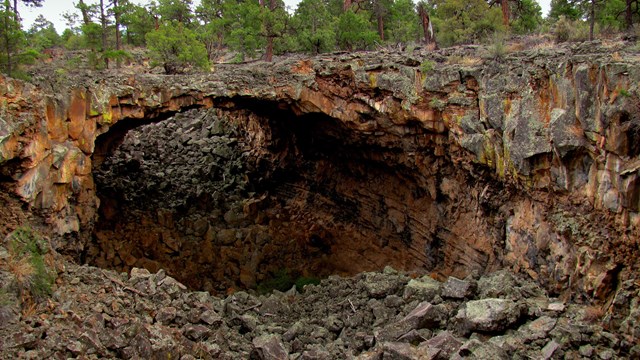 A bridge of dark brown lava rock crosses a deep trench filled with rubbly lava rock.