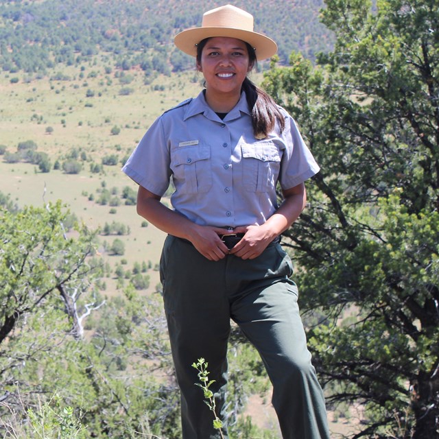 Park ranger wearing flat hat and uniform stands in front of desert landscape.