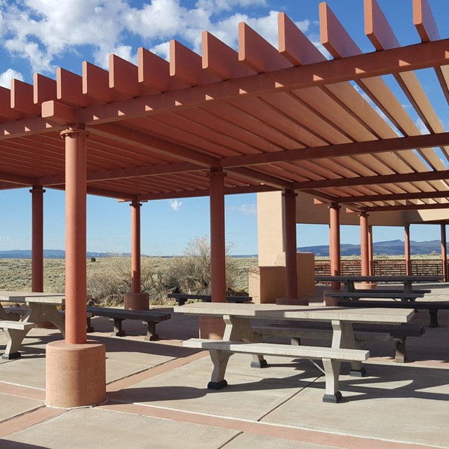 Picnic benches under a red awning on a concrete platform.