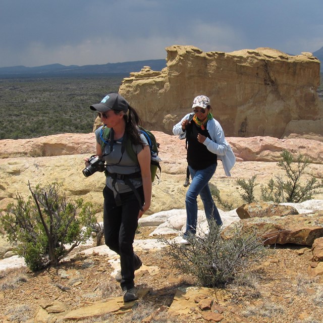 Two hikers walk across a sandstone trail.