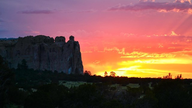 A sunset silhouettes a cliff. 