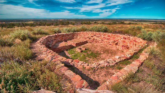 A circular kiva set in the ground against a clear sky.