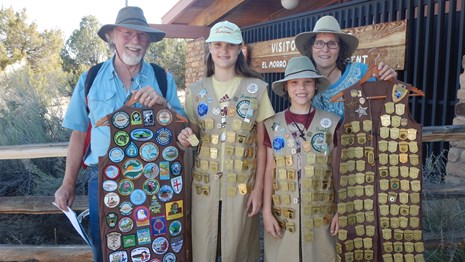 Two adults and two children display hundreds of Junior Ranger badges in the visitor center.