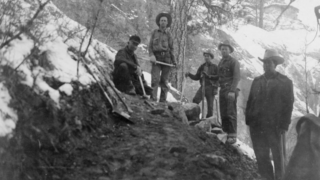 A group of five men in the process of digging out a new trail foundation.