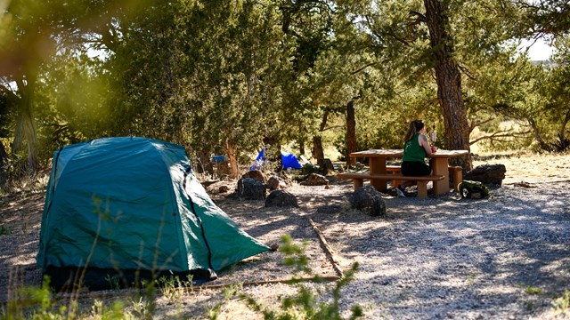 A visitor sits at the picnic area near her tent in the campground during summer.
