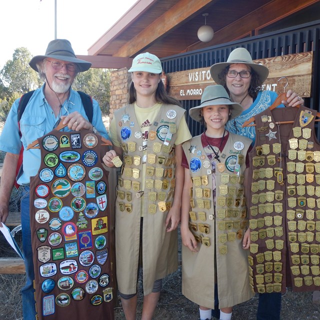 Two adults and two children display hundreds of Junior Ranger badges in the visitor center.