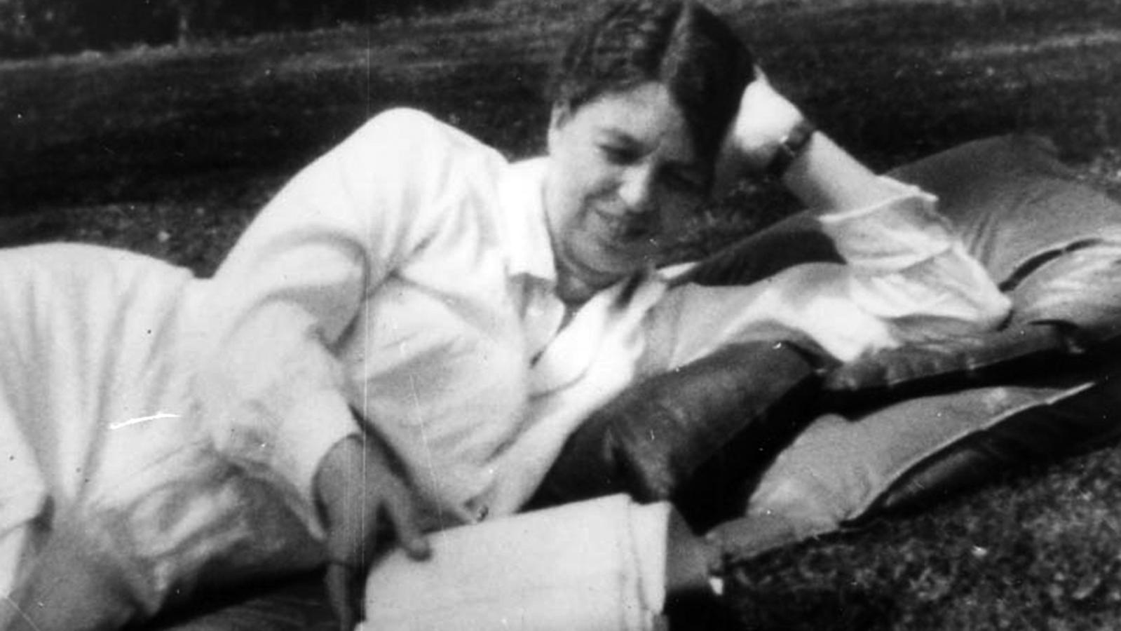 A woman in a white dress reclining on a lawn with a book.