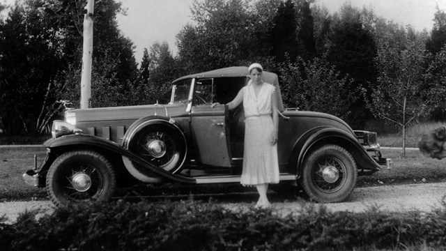 A woman in summer whites standing near an automobile.