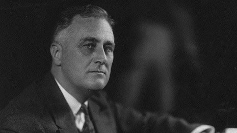 A man (FDR) in a suit seated at a desk with papers.