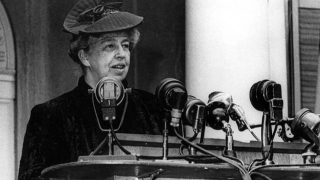 Eleanor Roosevelt speaking at a podium with many microphones.